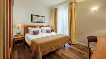 A hotel room with a large bed, wooden nightstands, a desk, and a chair.