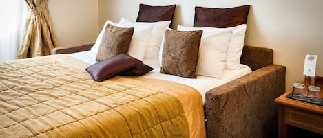 A neatly made bed with a patterned bedspread and pillows, a wooden headboard, and a bedside table with a glass and a small container.