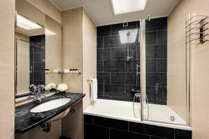 Un baño moderno con una pared de azulejos negros y beige, un lavabo blanco y una ducha con cerramiento de vidrio.