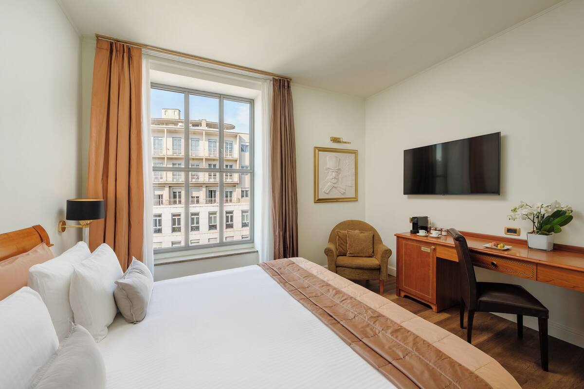 Una habitación de hotel con una cama grande, un escritorio, una silla, un televisor y una ventana con cortinas.