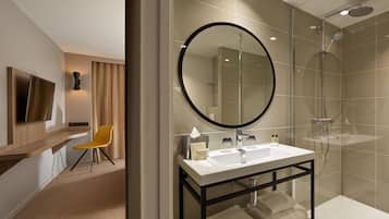 A modern bathroom with a large mirror, a shower, and a vanity with a sink.