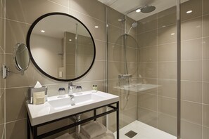 A modern bathroom with a round mirror, a sink, and a glass-enclosed shower. - Hôtel Auteuil Tour Eiffel (Paris)