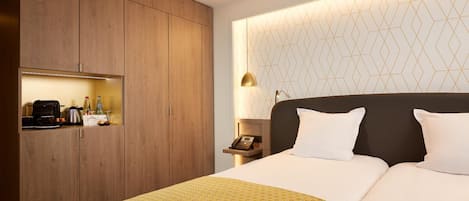 Habitación de hotel con una cama grande, armario de madera, mesita de noche con lámpara y pared con un estampado geométrico.