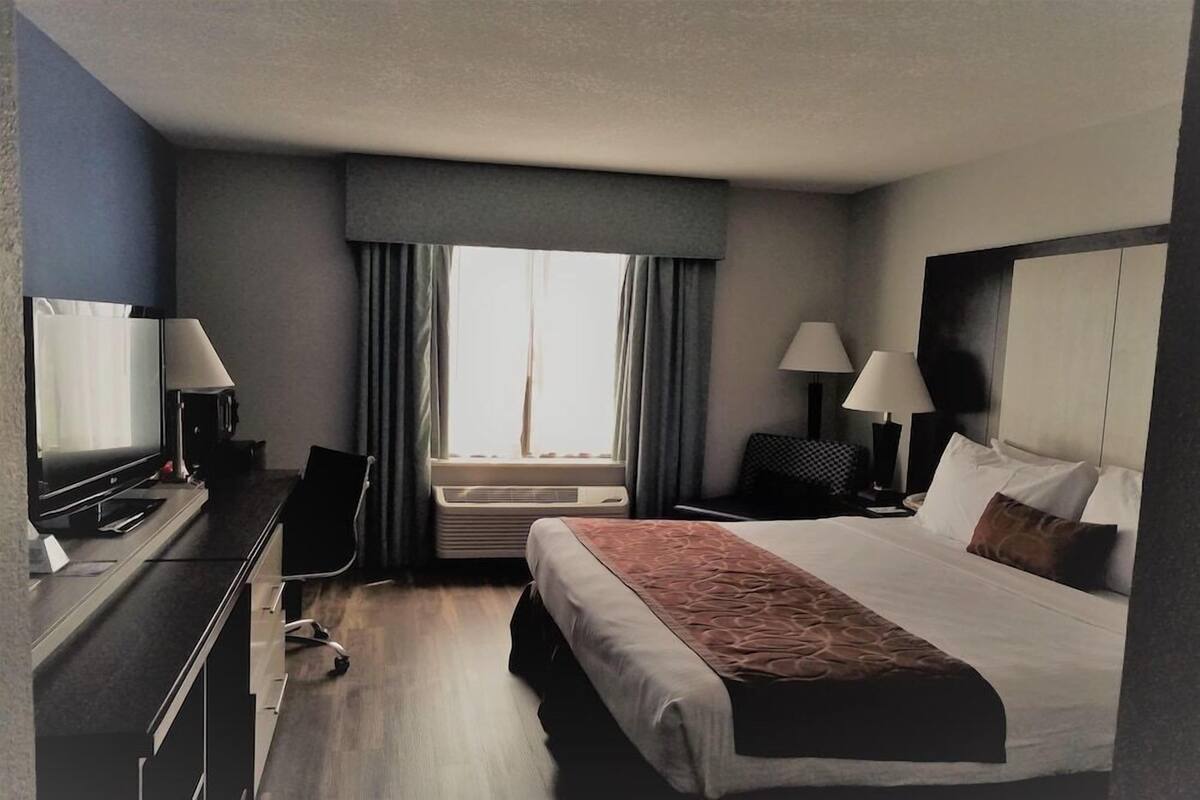 Habitación de hotel con cama, escritorio, silla, dos lámparas de noche y ventana con cortinas.
