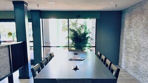 Un salón de conferencias con una larga mesa, sillas y una planta en maceta.