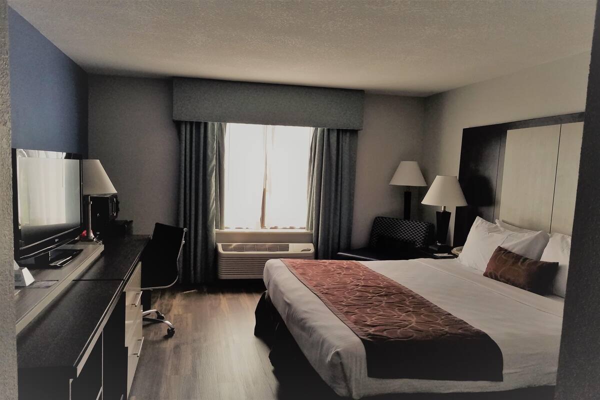 Habitación de hotel con cama, escritorio, silla, dos lámparas, televisión y aire acondicionado.