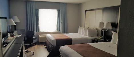 Une chambre d’hôtel avec deux lits, un bureau avec un ordinateur, une chaise, une fenêtre avec des rideaux et un grand miroir.