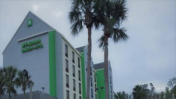 A Wyndham Garden Hotel building with a modern design, featuring a prominent green and white color scheme, and surrounded by palm trees.
