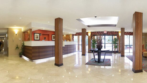 Un hall espacioso con mostrador de recepción, grandes columnas de madera y una mesa central con un florero.