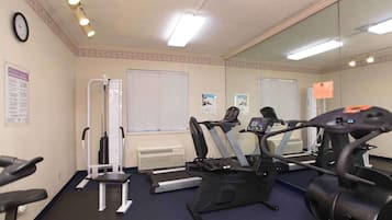 Een sportschool met trainingsapparatuur, een spiegel en een klok aan de muur.