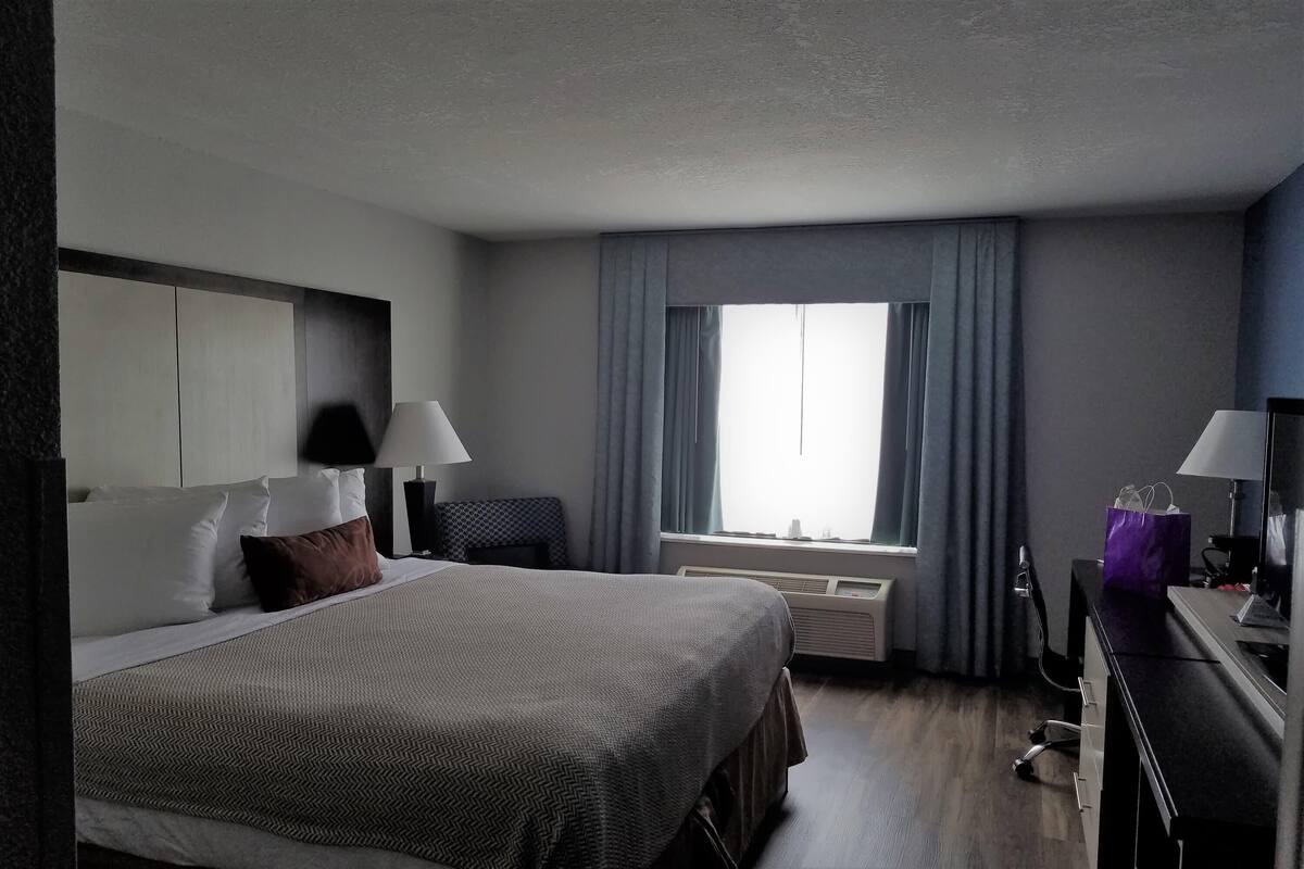 Habitación de hotel con cama, mesitas de noche, escritorio, silla, ventana con cortinas y aire acondicionado.