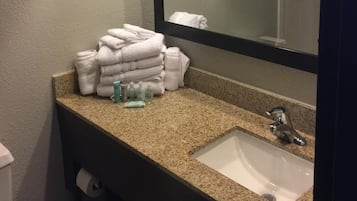 A bathroom with a granite countertop, a white sink, a mirror, and a stack of white towels.