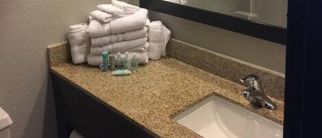Un baño con encimera de granito, un lavabo blanco, un espejo y una pila de toallas blancas.