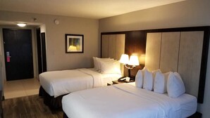 Habitación de hotel con dos camas, una mesita de noche con lámpara, un cuadro en la pared y una puerta a la izquierda.
