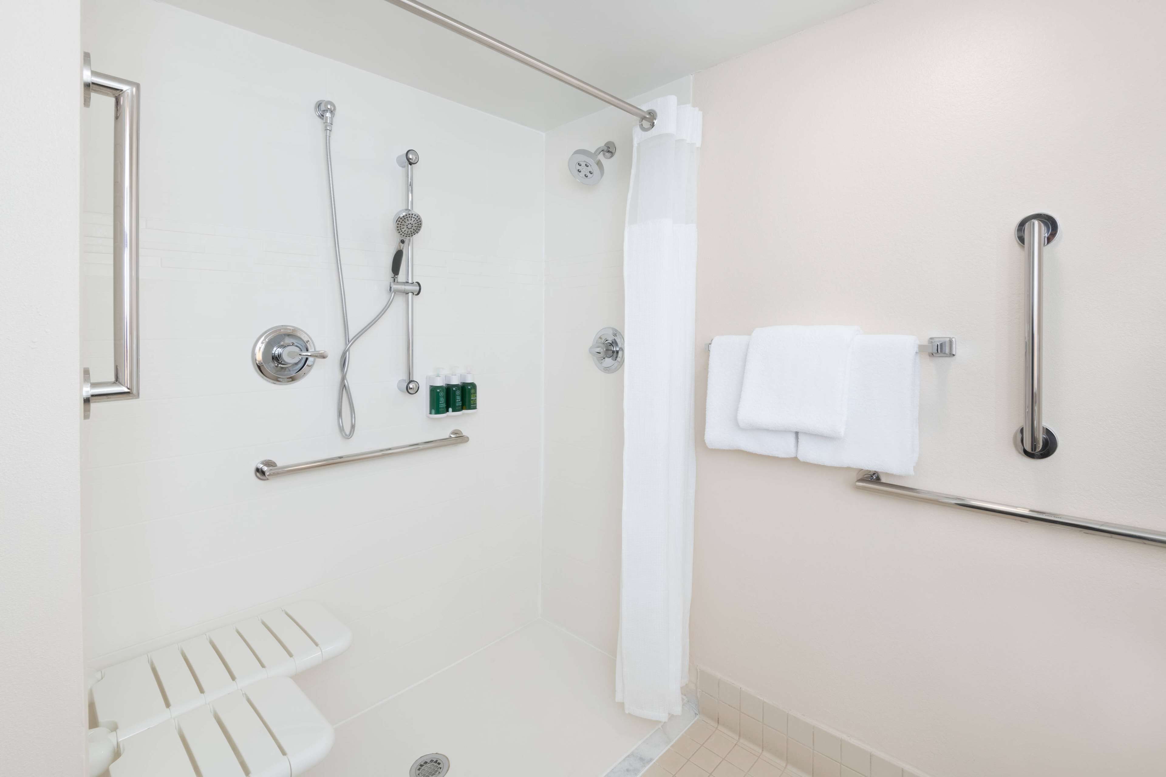 A bathroom with a shower, grab bars, a towel rack, and a toilet with a handrail.
