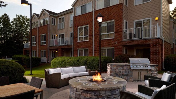 An outdoor patio with a stone fire pit, wicker furniture, and a grill.