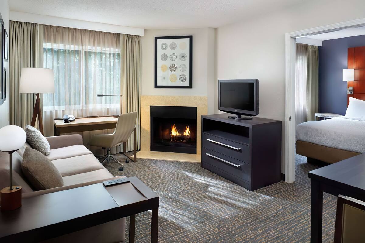 Een hotelkamer met een bank, bureau, televisie, open haard en een bed.