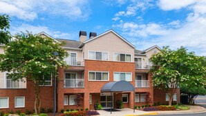 A multi-story residential building with a brick facade, a covered entrance, and a landscaped front yard.