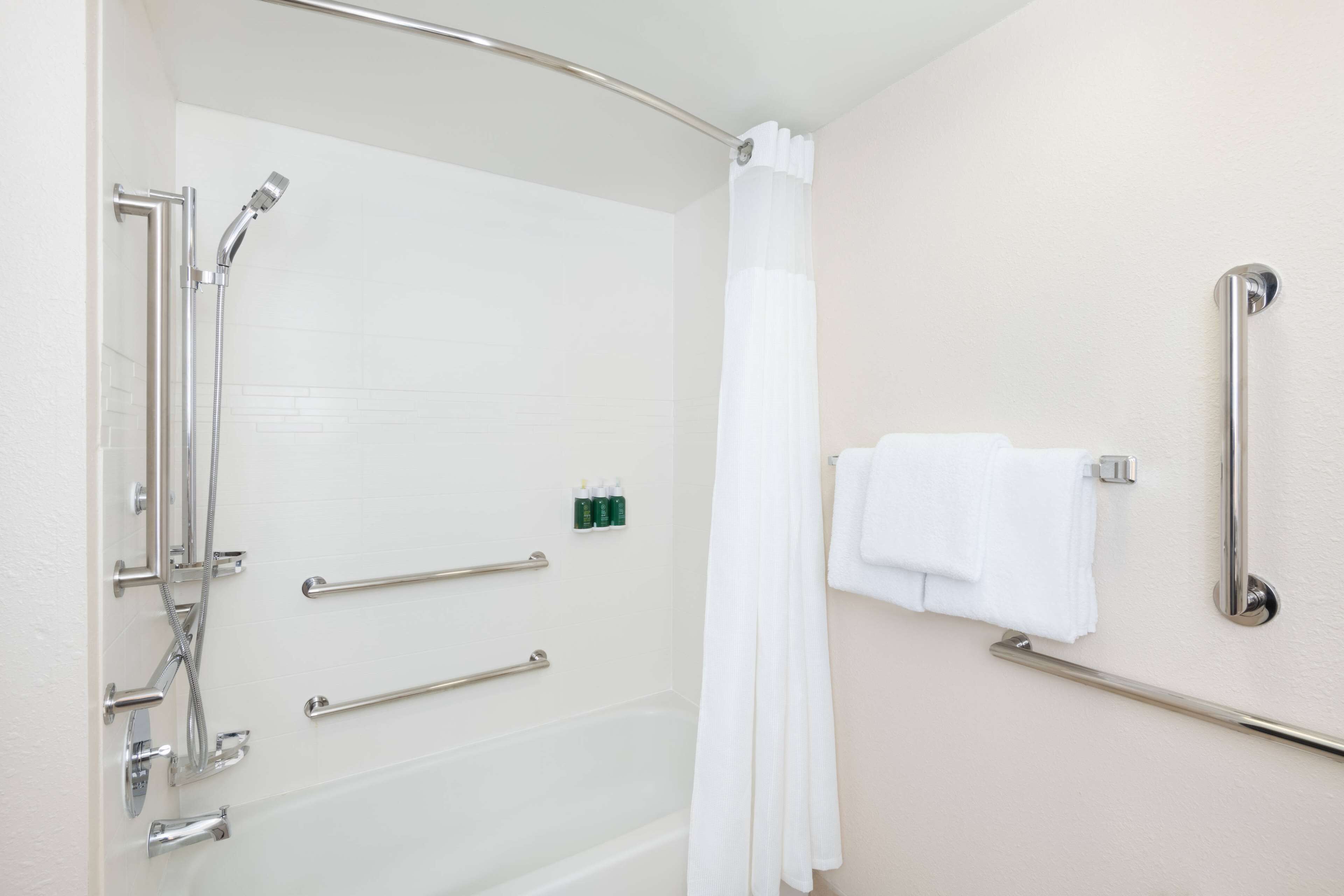 A bathroom with a shower, grab bars, a bathtub, and a towel rack.