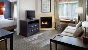 A hotel room with a bed, a TV, a fireplace, a desk, and a sofa.