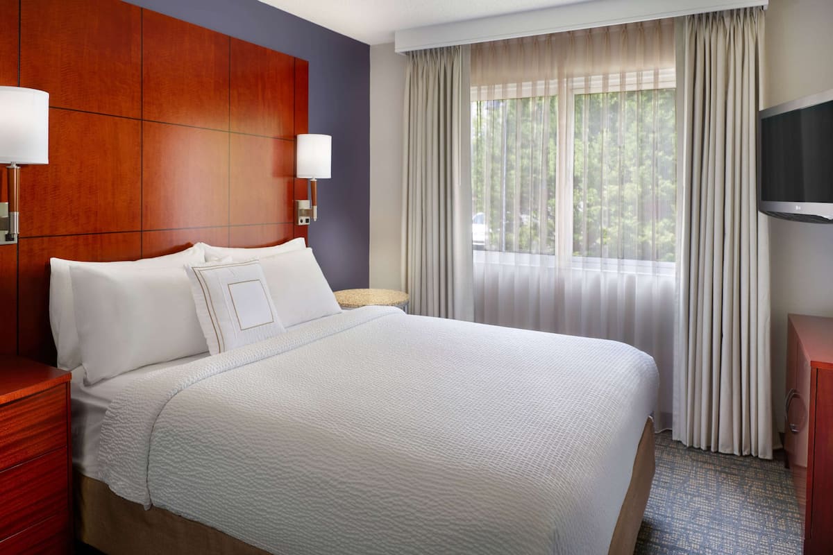 Hotelkamer met een groot bed, houten hoofdeinde, een televisie en een raam met gordijnen.