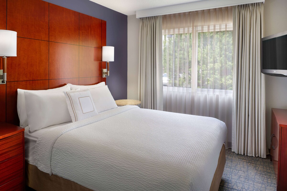 A hotel room with a large bed, a wooden headboard, a TV, and a window with curtains.