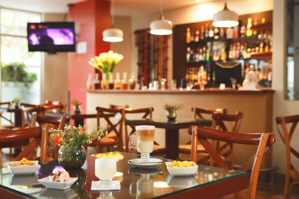 Ein Restaurant mit Barbereich, Holzhockern, einem Glastisch und einem an der Wand befestigten Fernseher.