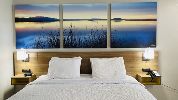 A hotel room with a large bed, two bedside tables, a nightstand, a wall-mounted phone, and a painting of a landscape. - Days Inn by Wyndham Killeen Fort Hood (Killeen)