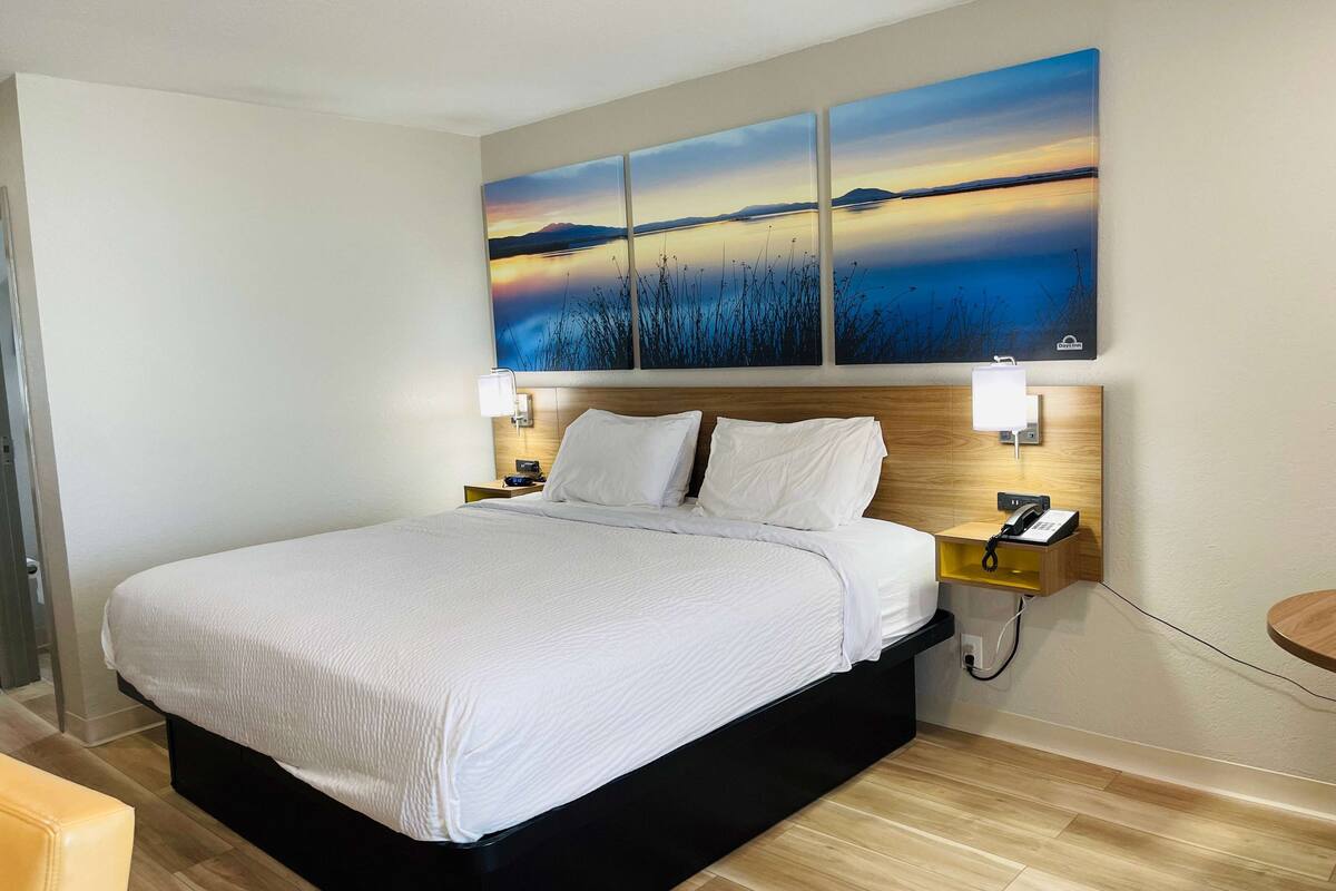 A hotel room with a large bed, two bedside tables, a nightstand, a wall-mounted phone, and a painting above the bed.