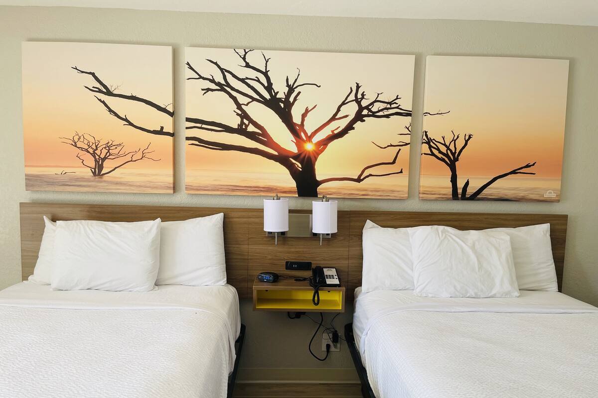 A hotel room with two beds, a nightstand with a lamp, and a wall-mounted phone.