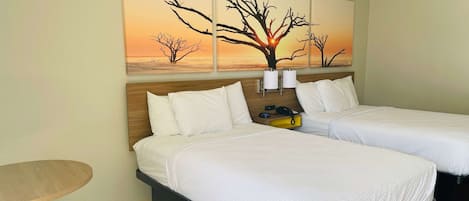 A hotel room with two beds, a small table, and a wall-mounted lamp.