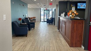 A reception area with a wooden counter, blue chairs, and a TV screen. - Days Inn by Wyndham Killeen Fort Hood (Killeen)