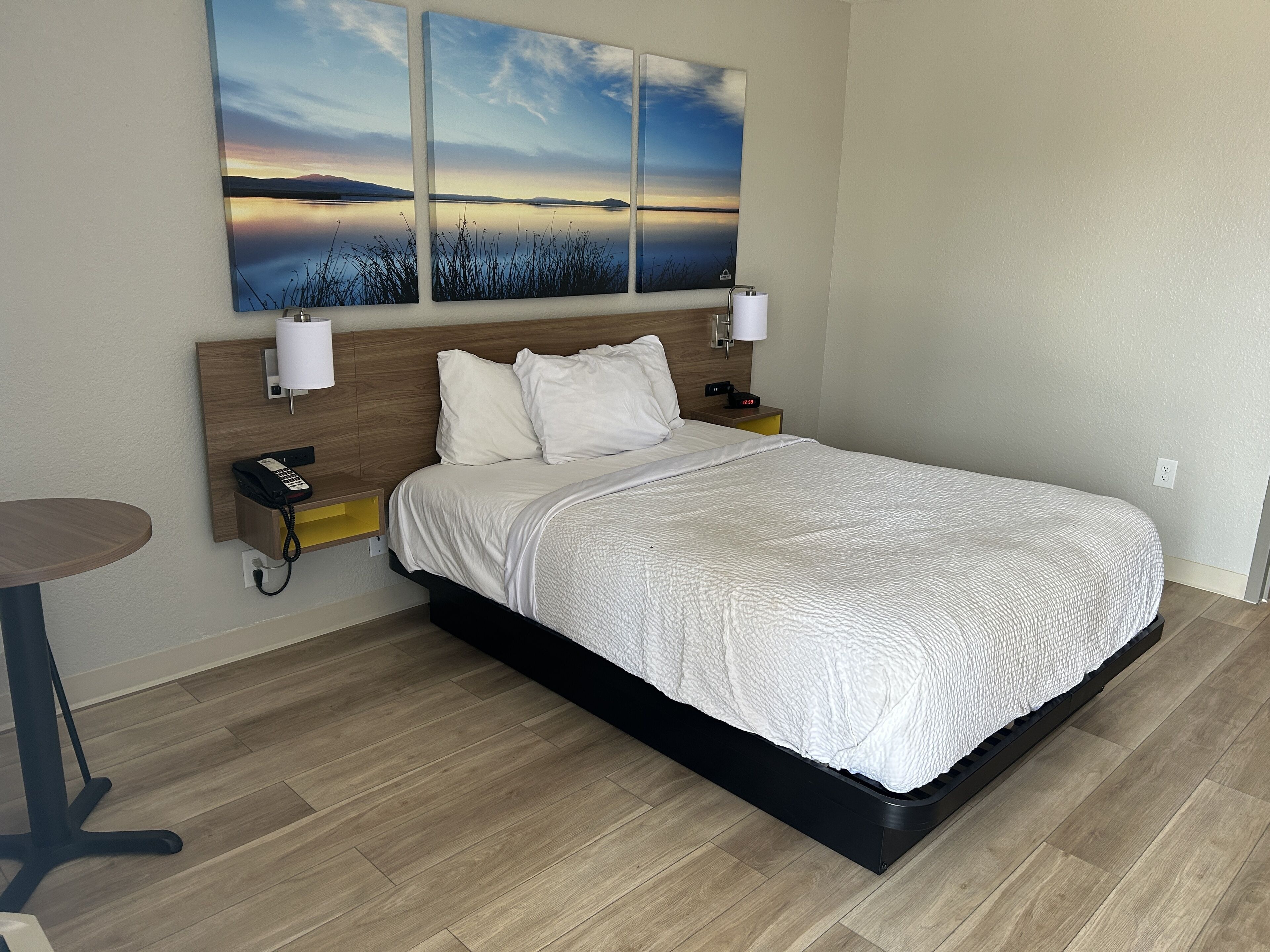 A hotel room with a bed, bedside tables, a wall-mounted phone, and a painting of a landscape.