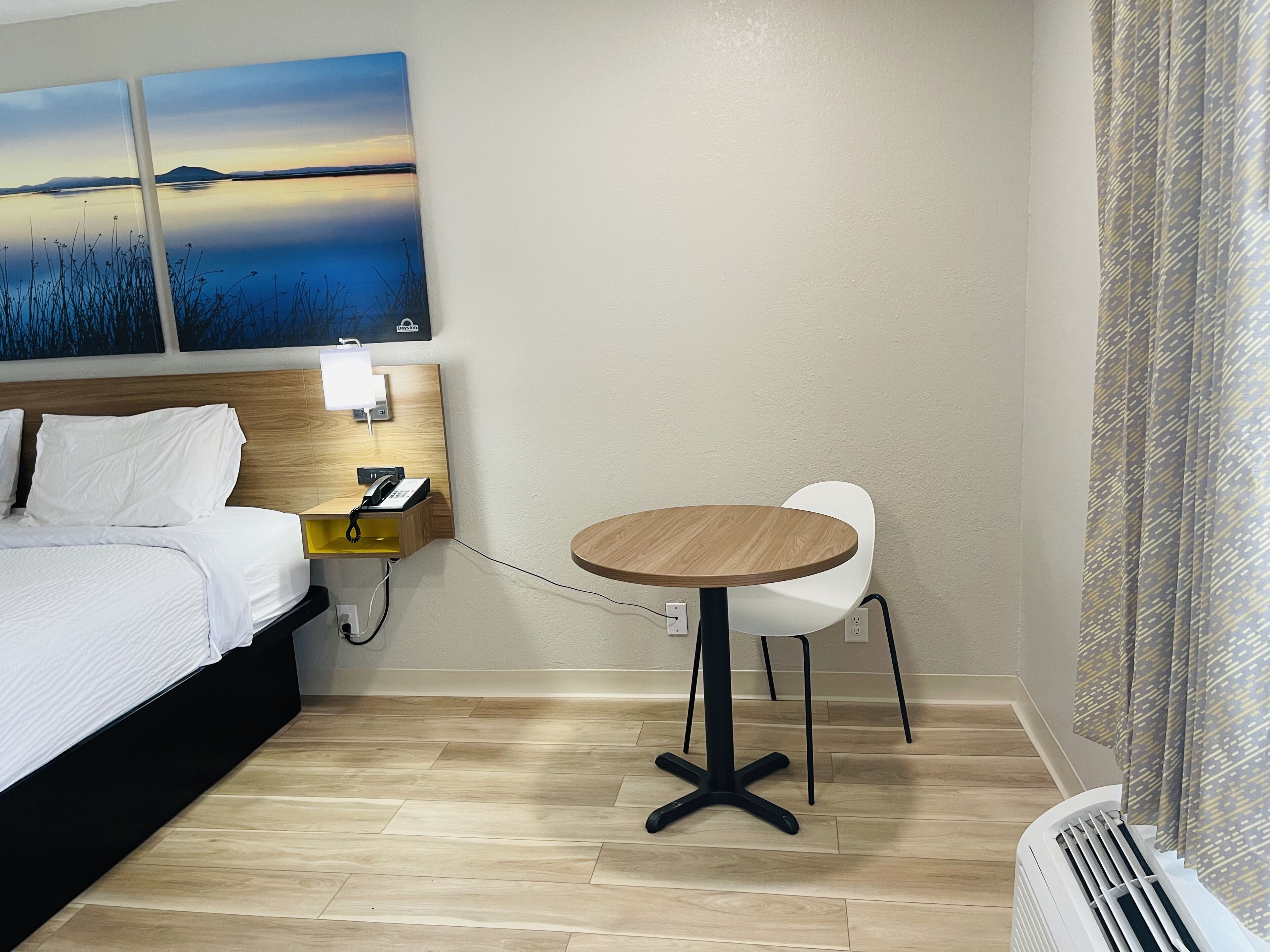 A hotel room with a bed, bedside table, phone, and a small round table with chairs.
