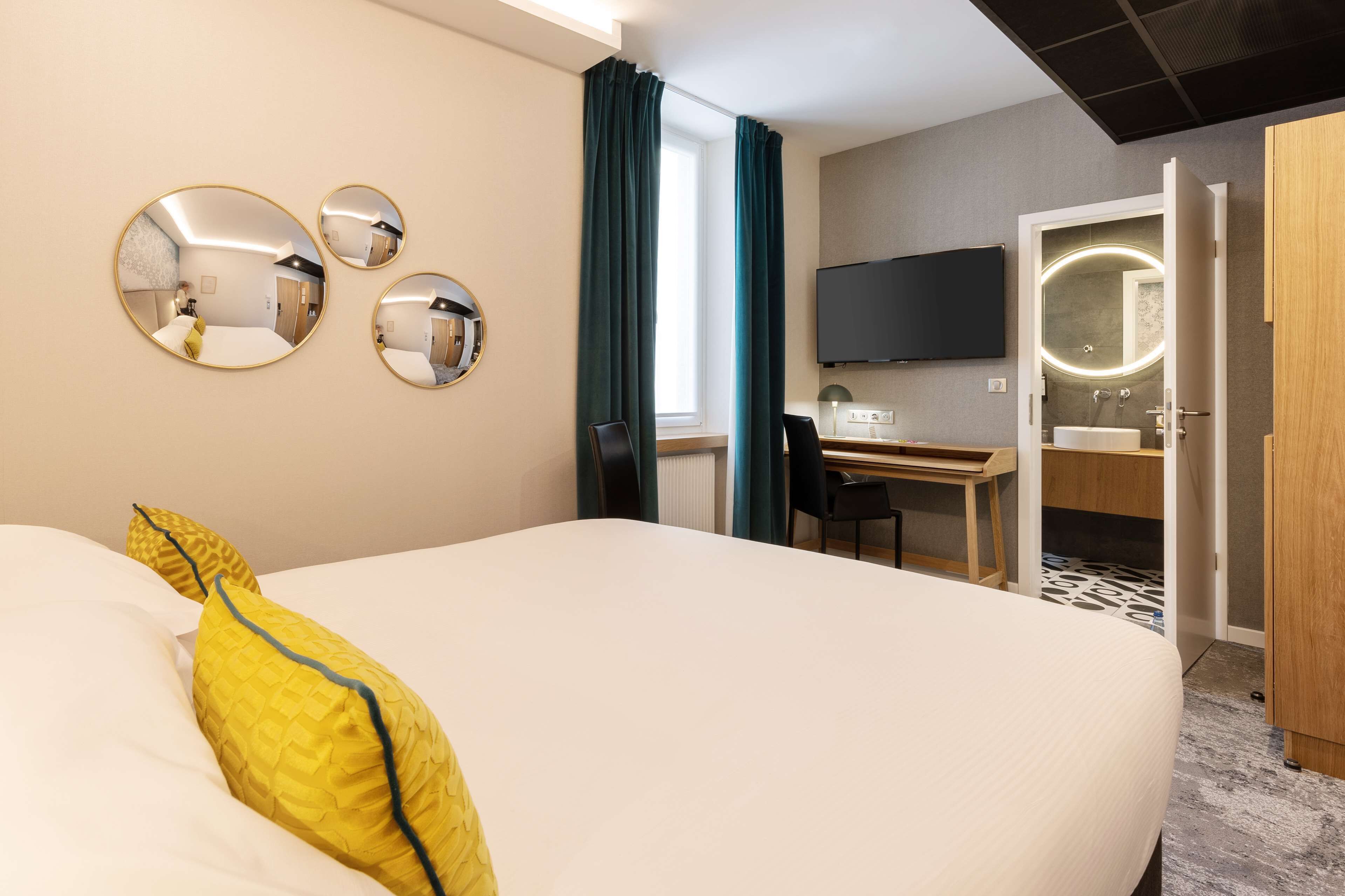 A hotel room with a large bed, a desk with a chair, a TV, and a bathroom with a mirror.