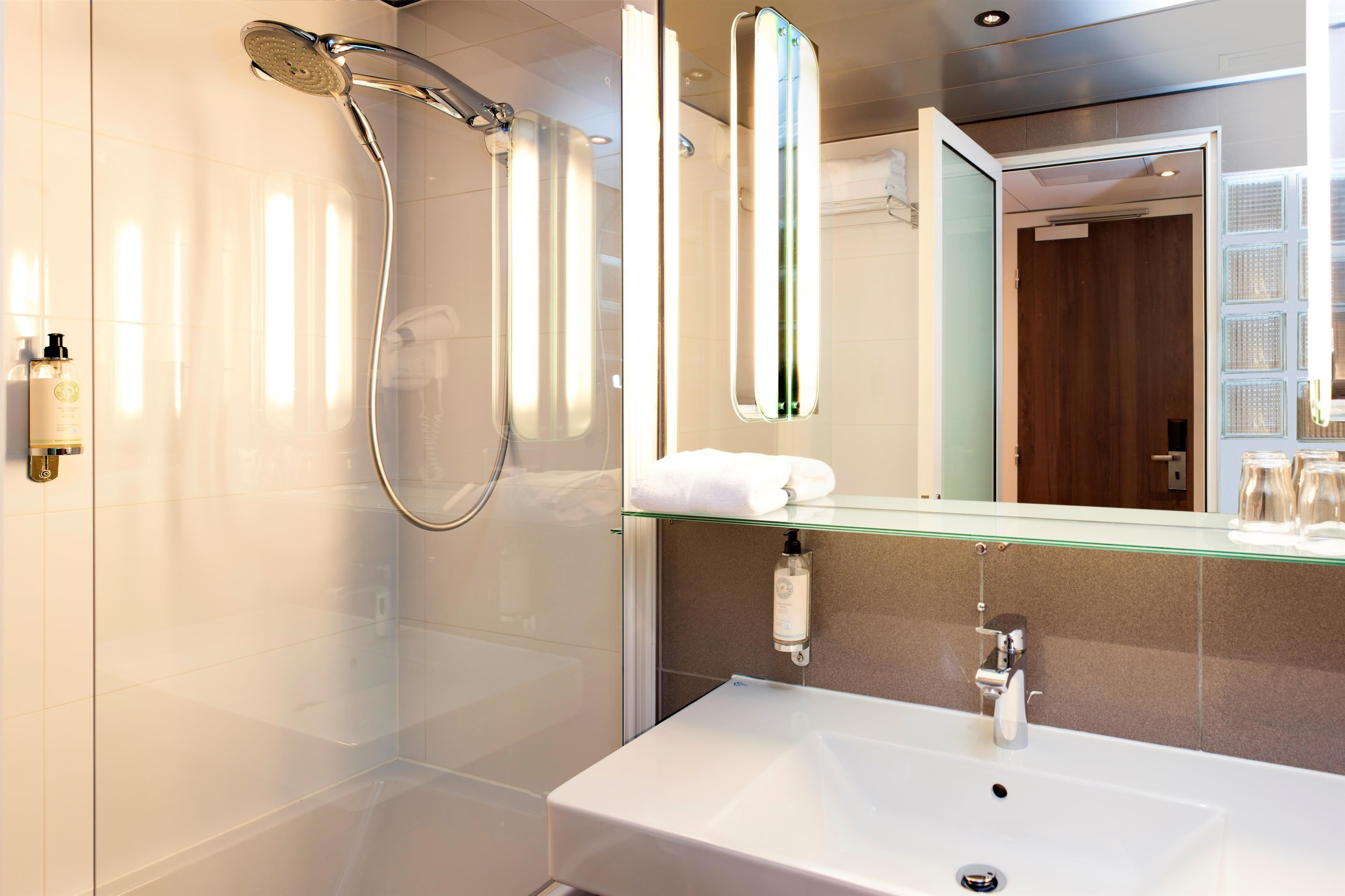 A modern bathroom with a glass-enclosed shower, a white sink, and a mirror with a glass shelf above it.