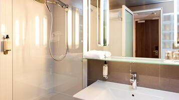 A modern bathroom with a glass-enclosed shower, a white sink, and a mirror with a glass shelf above it.
