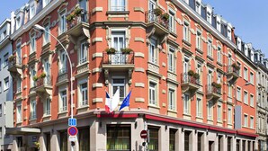 A multi-story hotel with a red facade, multiple balconies with flower boxes, and flags.