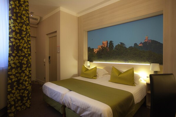 A hotel room with a large bed, two pillows, a nightstand, a chair, and a wall-mounted lamp. - Best Western Plus Monopole Metropole (Strasbourg)