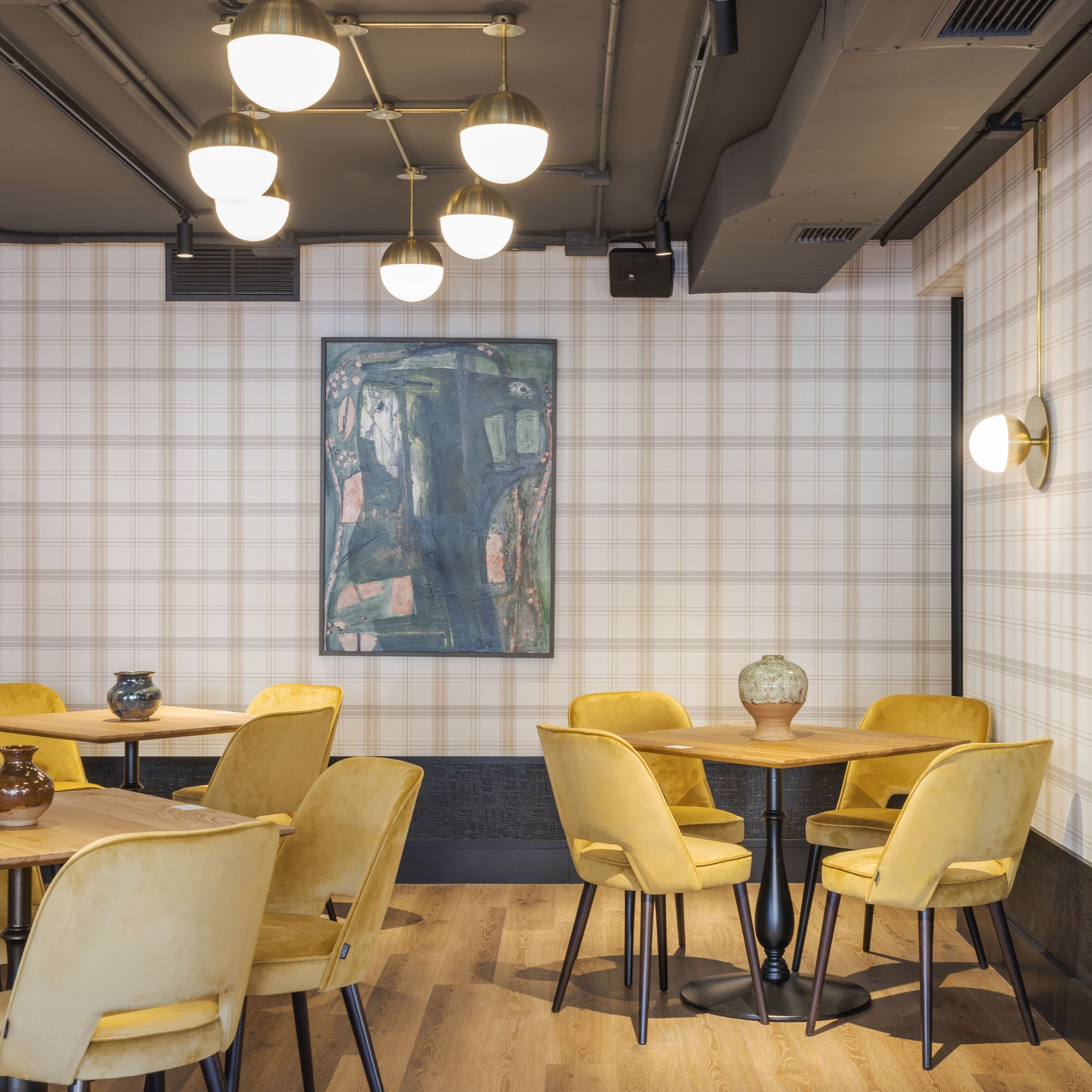 A restaurant interior with a modern design, featuring yellow chairs, wooden tables, and a large abstract painting on the wall.