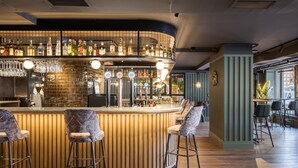 A bar area with a curved counter, multiple stools, and a variety of bottles and glasses.