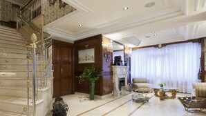 A grand lobby with a marble staircase, a fireplace, and a seating area with sofas and a coffee table.