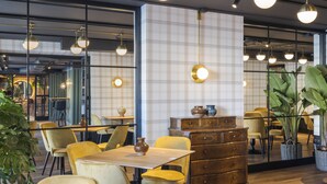 A modern restaurant interior with wooden tables, yellow chairs, and pendant lighting.