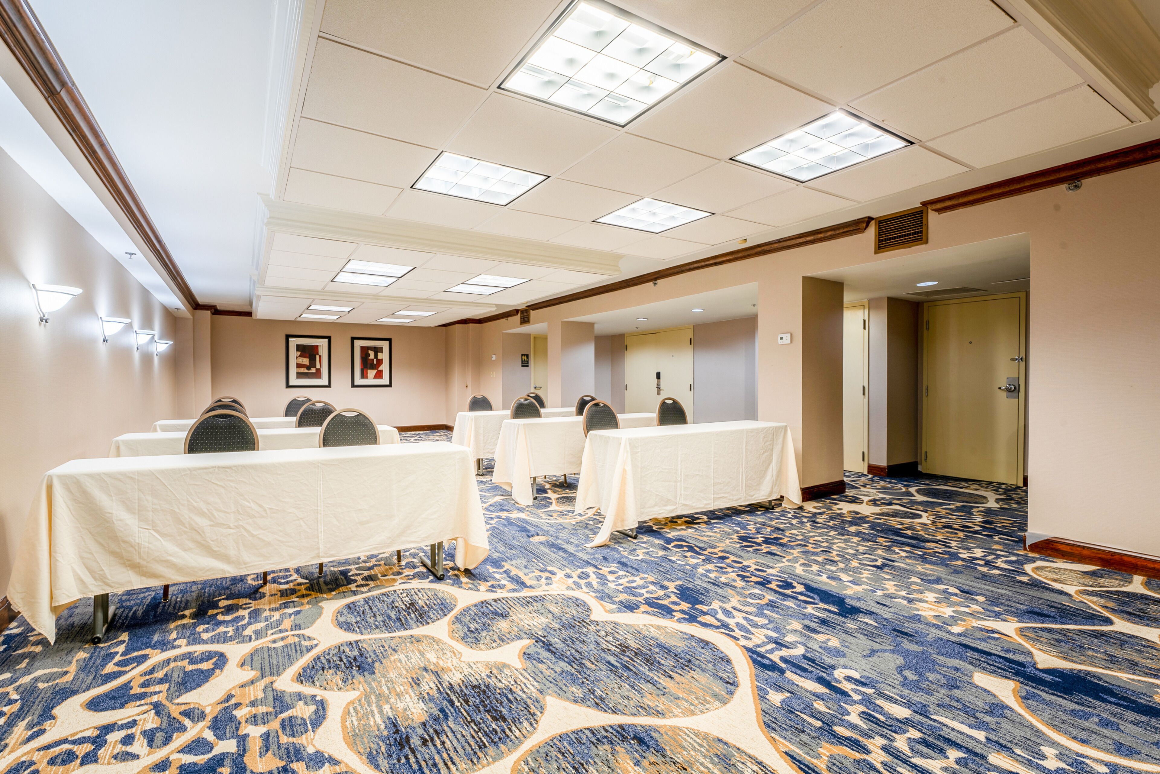 A conference room with tables and chairs, a patterned carpet, and a door in the background.