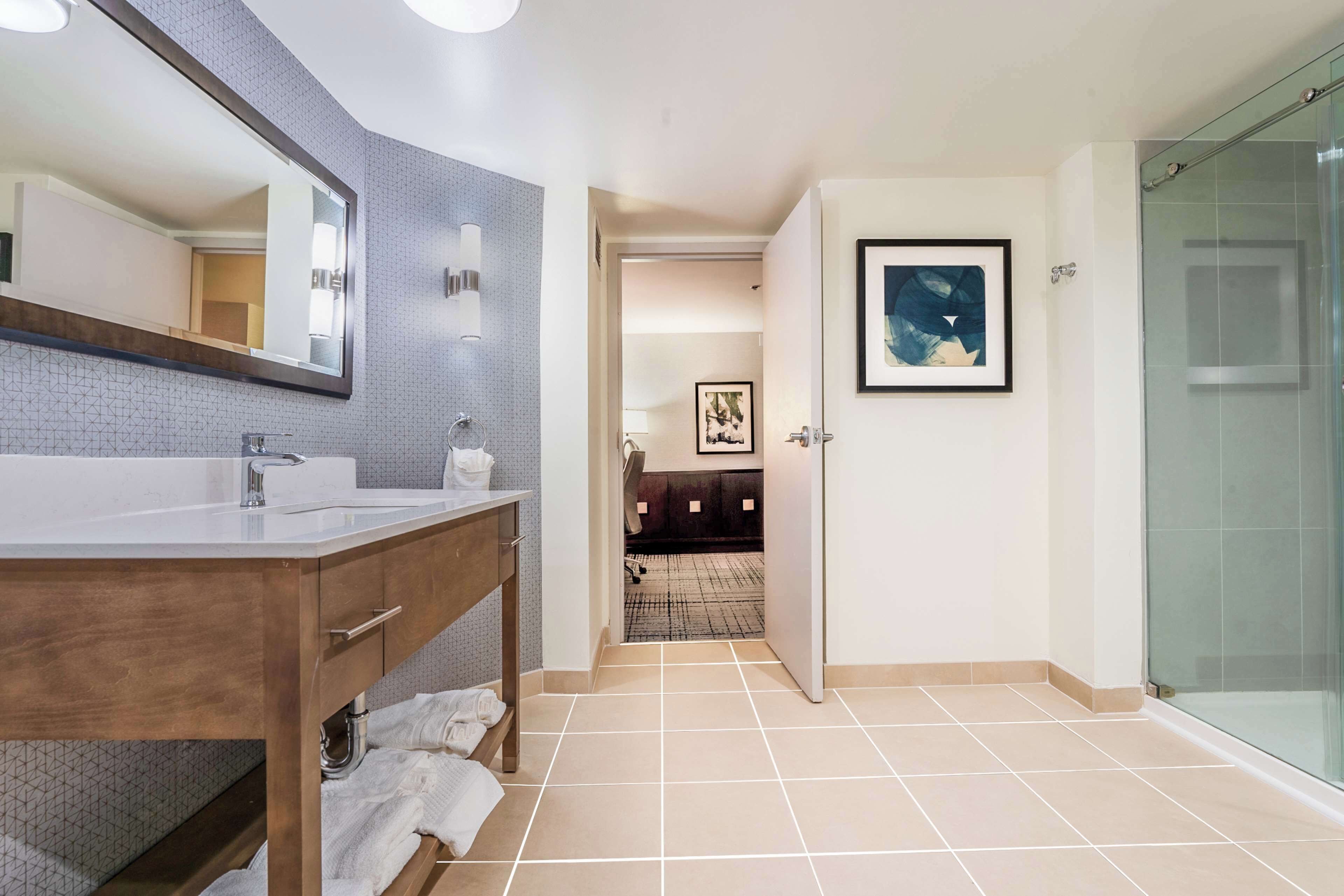 Un baño moderno con un espejo grande, dos lavamanos, un mueble de tocador de madera y una cabina de ducha de vidrio.