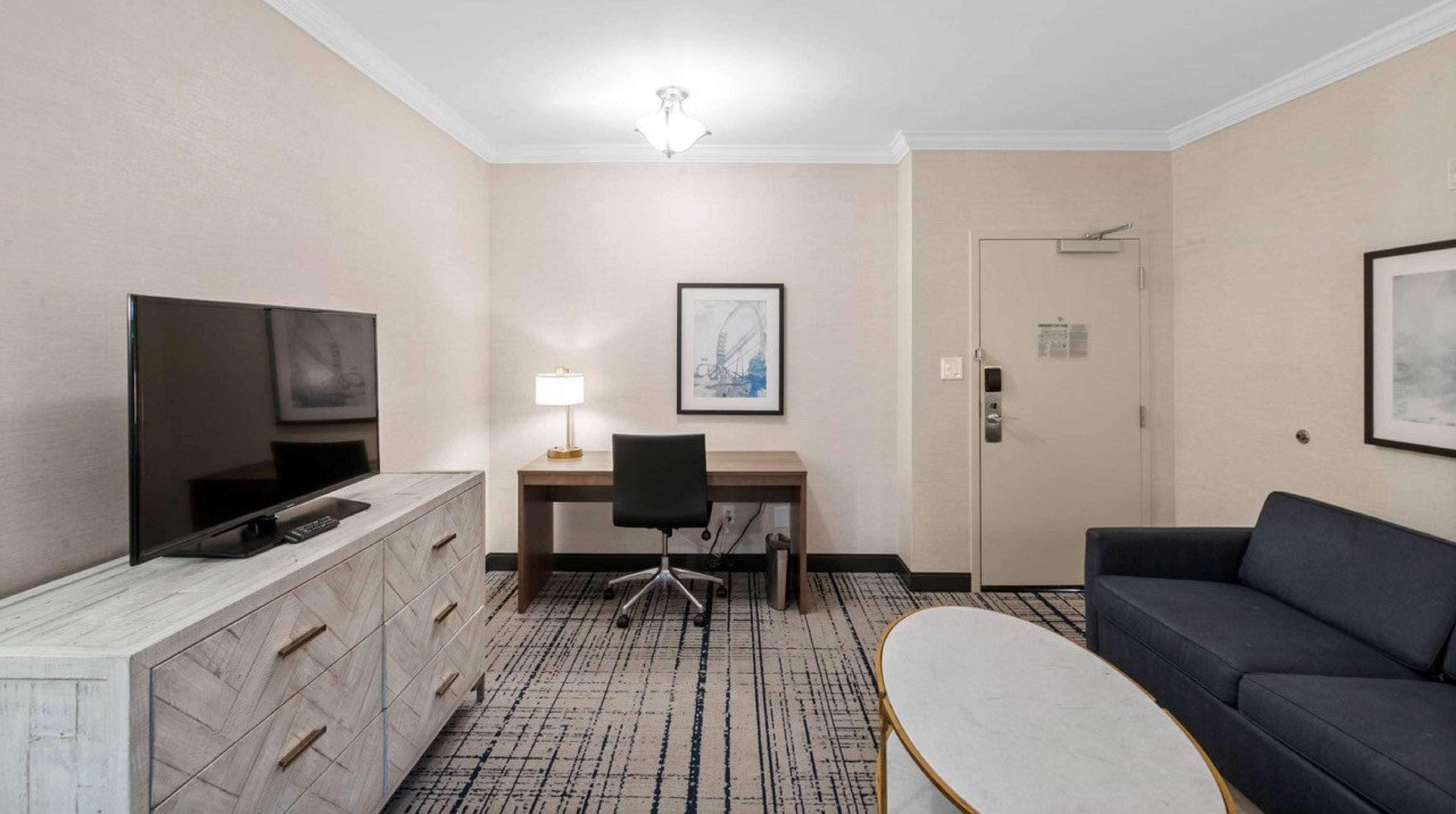 Habitación de hotel con televisión de pantalla plana, un escritorio con silla, un sofá y un cuadro en la pared.