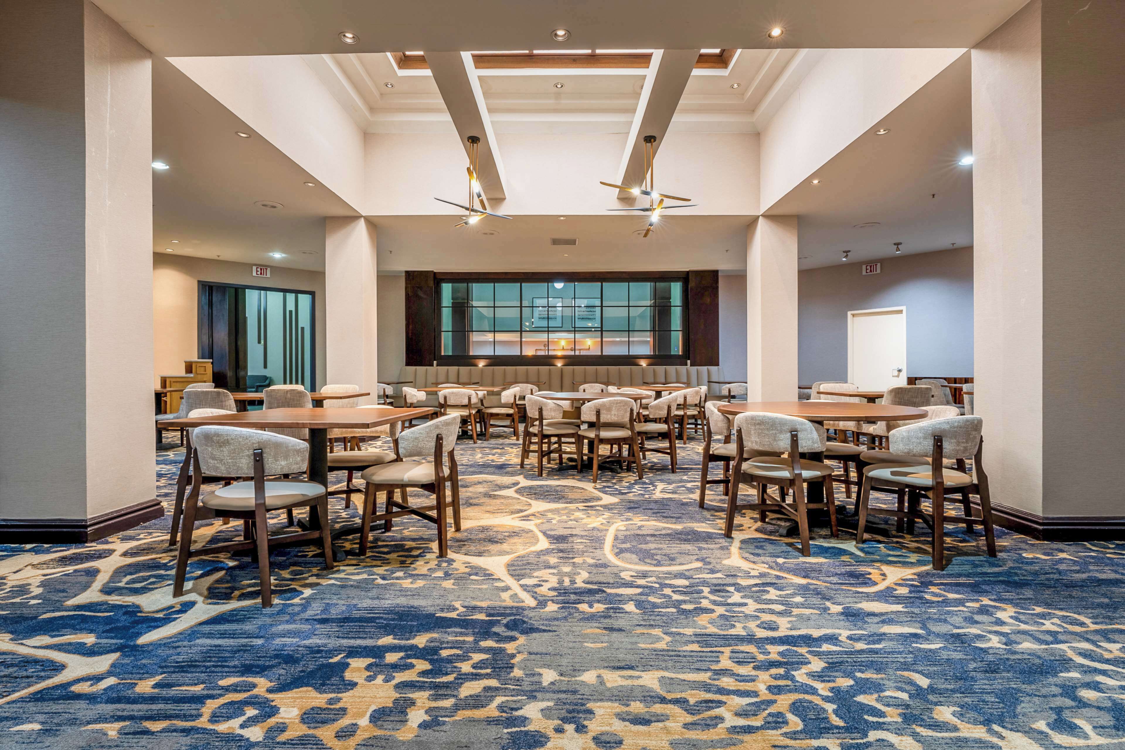 A conference room with multiple tables and chairs, a patterned carpet, and a large window with a view.