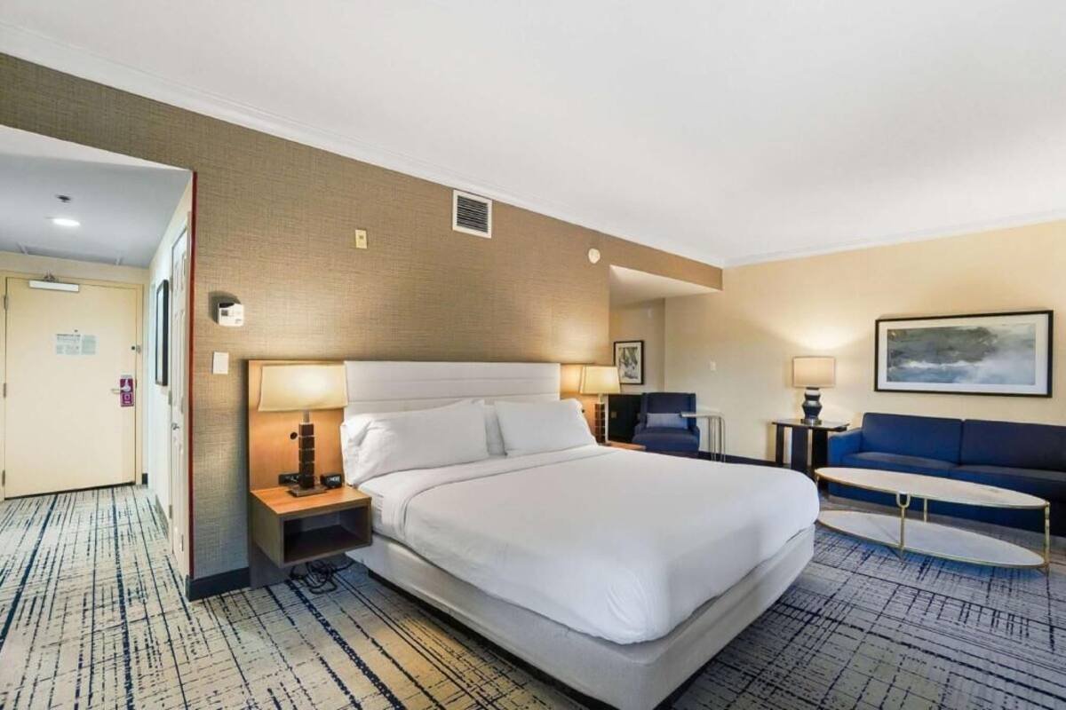 A hotel room with a large bed, a sofa, a small table, and a painting on the wall.