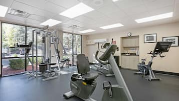 A gym with various exercise equipment, large windows, and a clock on the wall.