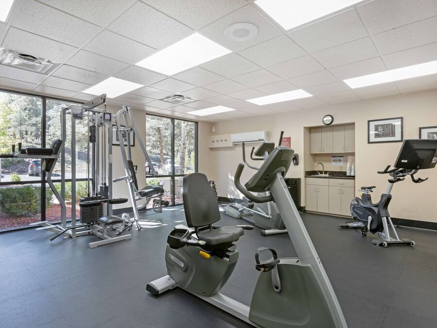A gym with various exercise equipment, large windows, and a clock on the wall.